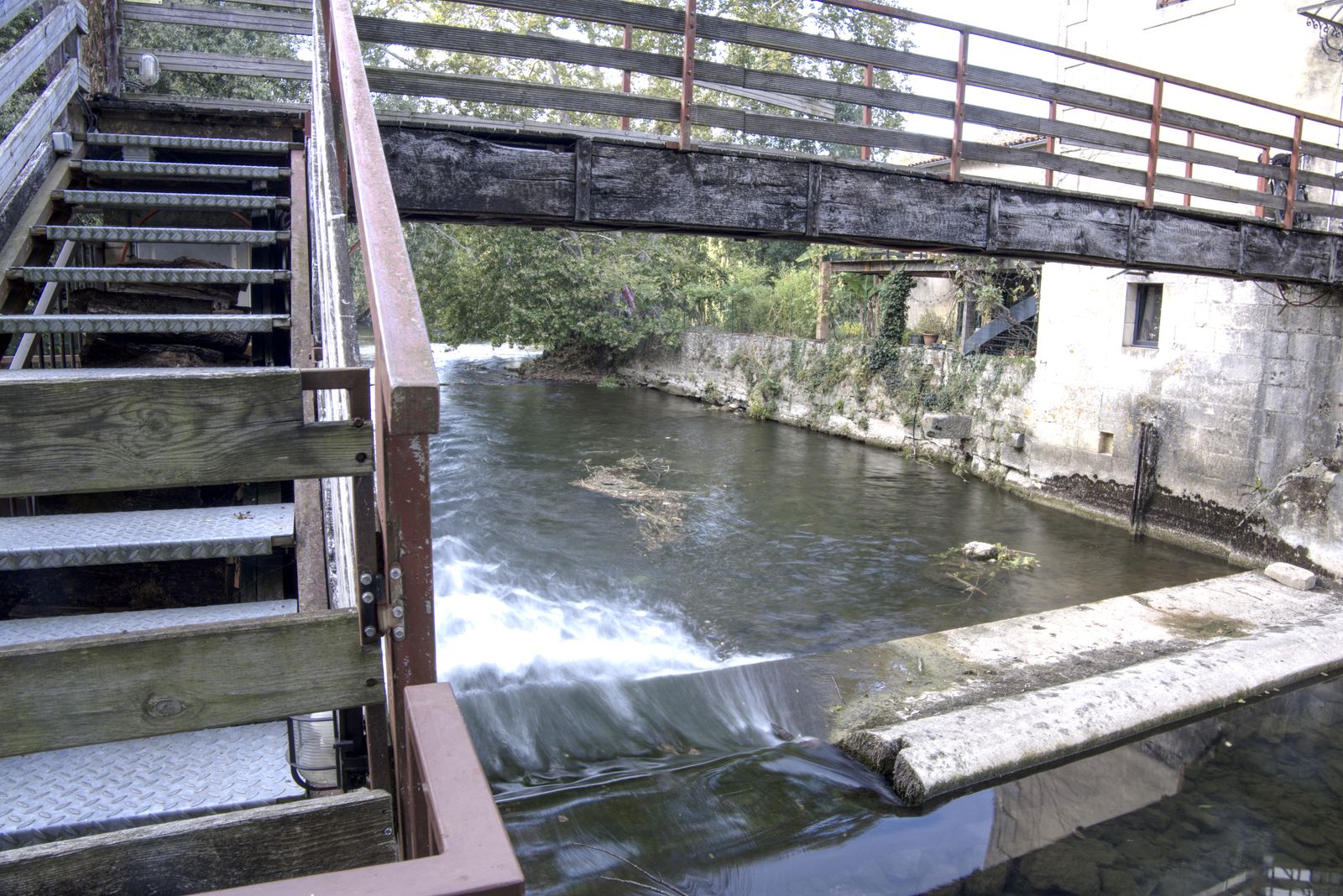 Déversoir de rivière sous une passerelle en bois près d'un ancien moulin