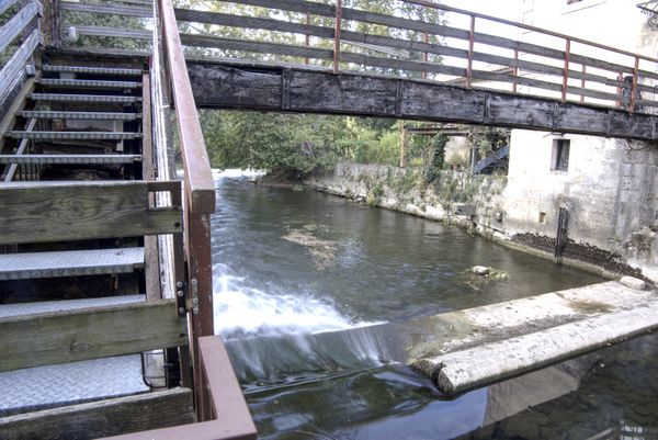 Déversoir de rivière sous une passerelle en bois près d'un ancien moulin