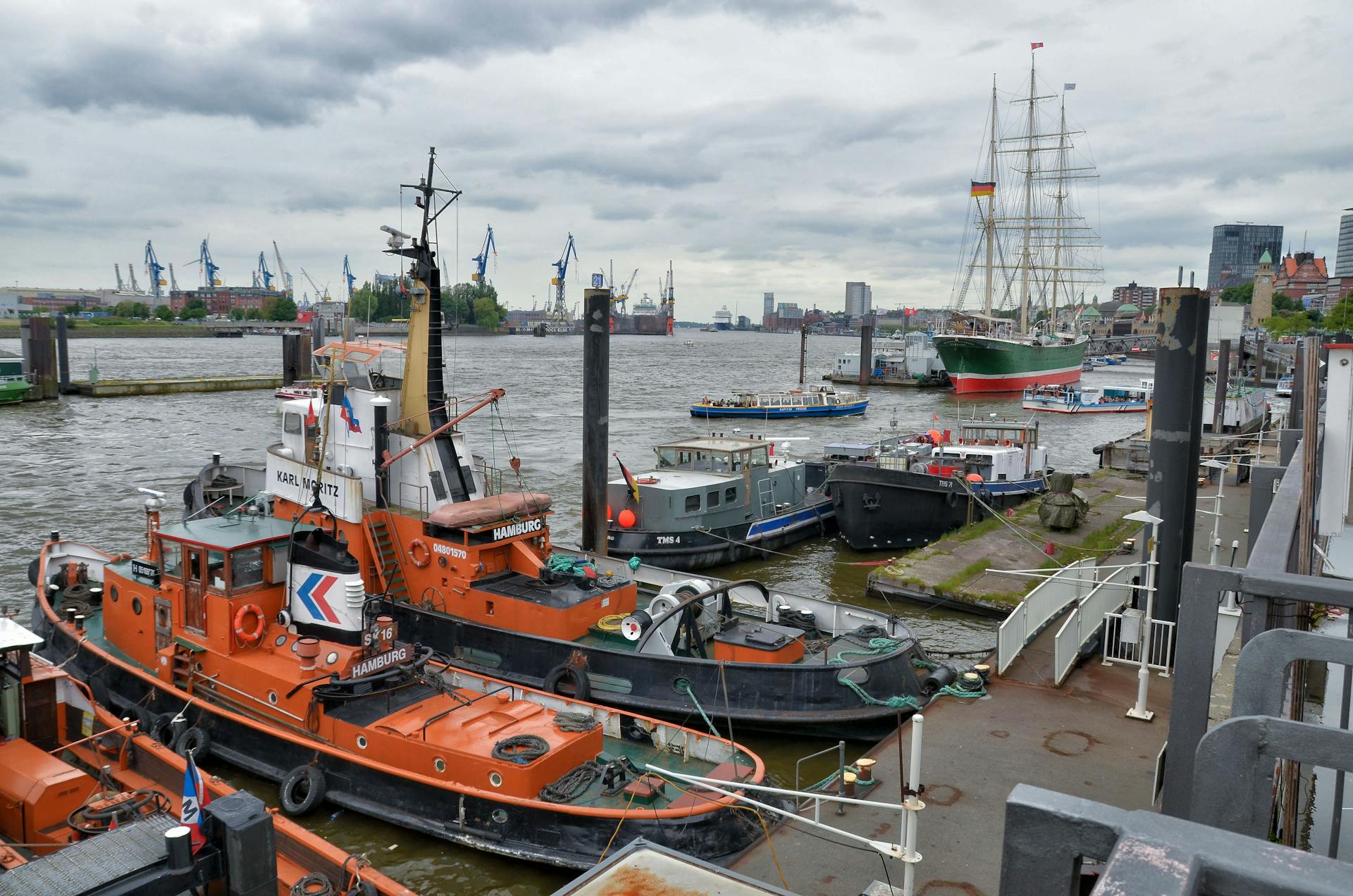 Tugboats and ships moored in Hamburg harbor under cloudy skies, a hub of maritime activity.