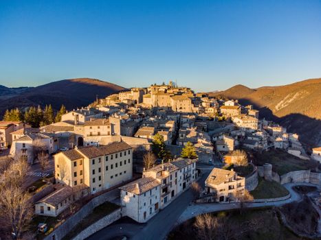 Aerial shot of a medieval Italian village with stone buildings and hills under a clear blue sky. — photo by jonathan emili
