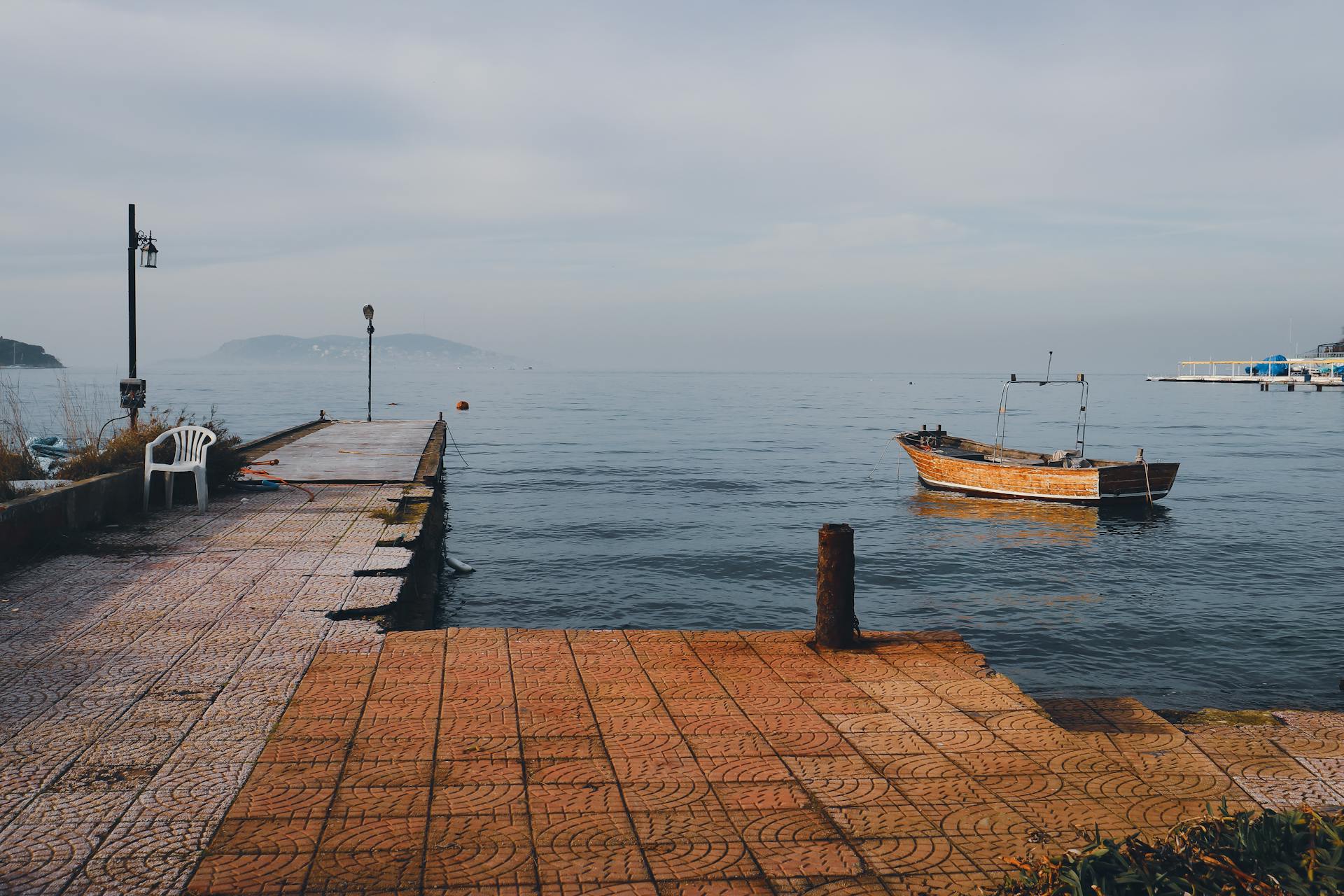 A tranquil scene of an old dock and wooden boat on a calm sea under a cloudy sky.