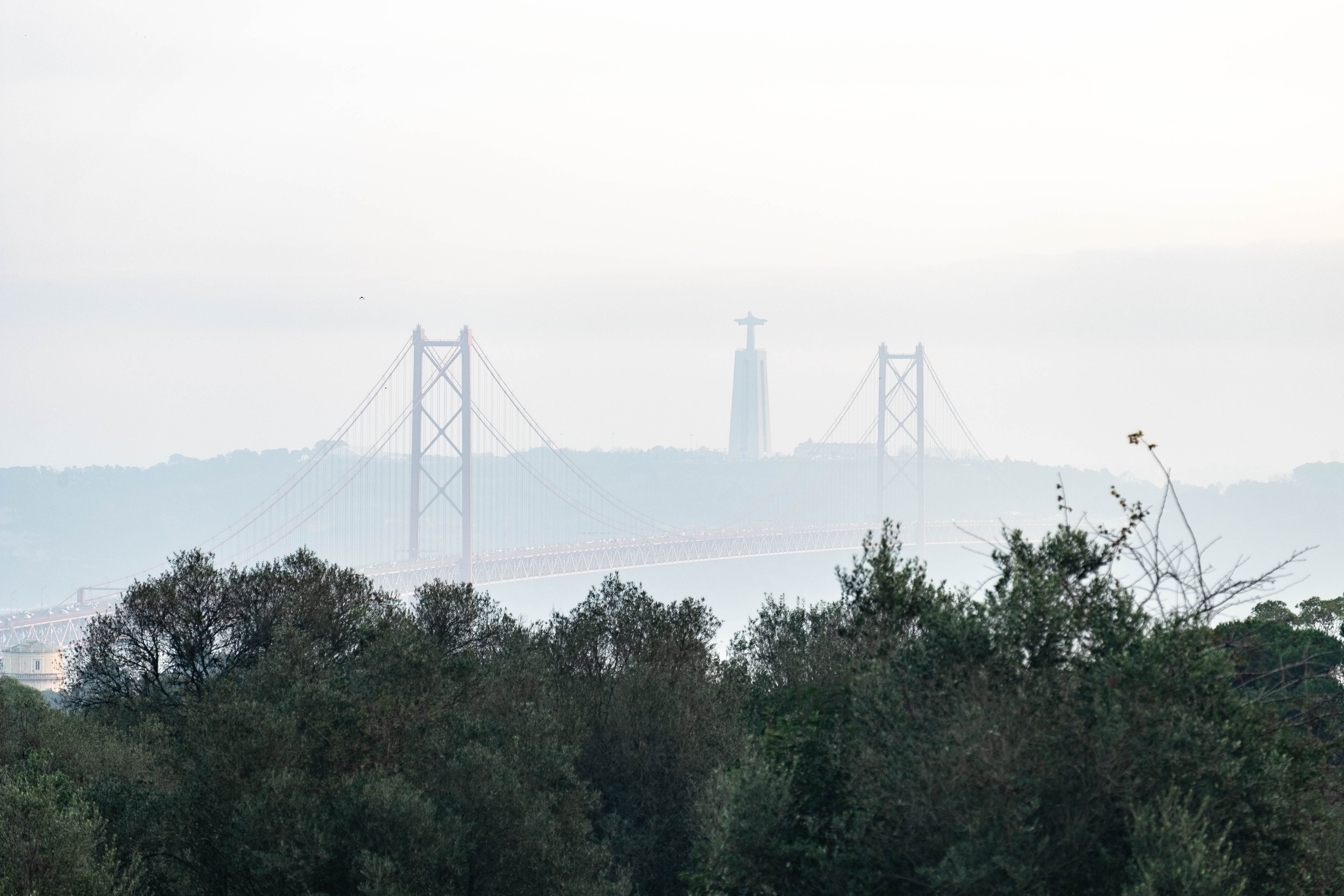 A foggy landscape of the 25 de Abril Bridge and Cristo Rei statue in Lisbon.