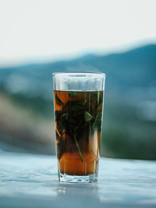 Free A glass of refreshing Moroccan mint tea with fresh herbs, set against a serene mountain backdrop, captured outdoors. Stock Photo