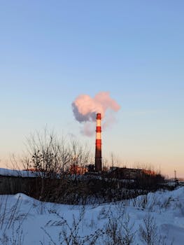A smokestack emitting smoke in an industrial area during winter.