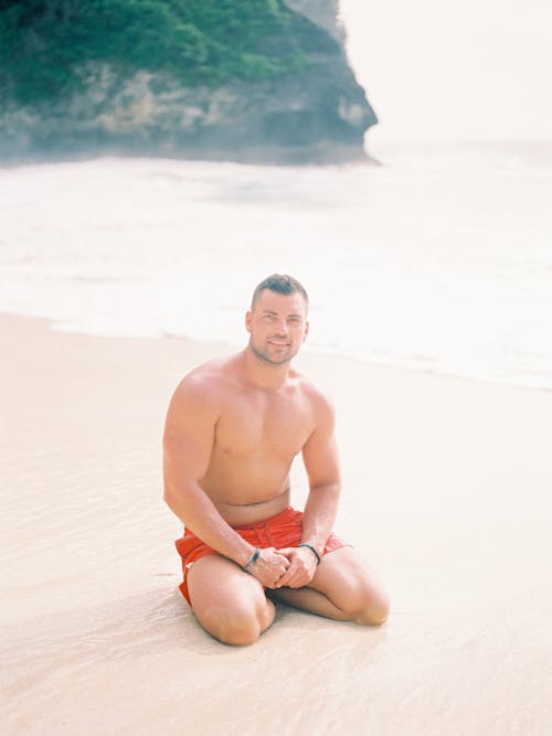 Man in Swimming Shorts Sitting on Beach 