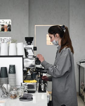 Barista wearing a mask making coffee with an espresso machine in a contemporary cafe setting.