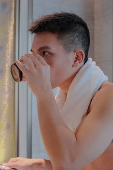 Portrait of a young man drinking water indoors with a towel around his neck.