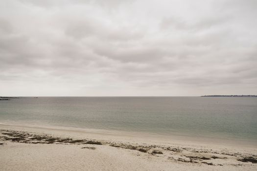 A serene beach scene with a calm sea and overcast sky creating a tranquil atmosphere.