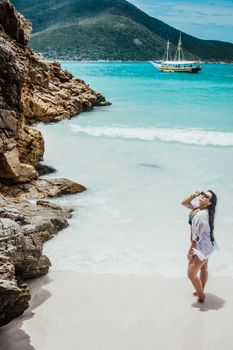 Young woman in white shirt posing by the ocean on a sunny tropical beach.