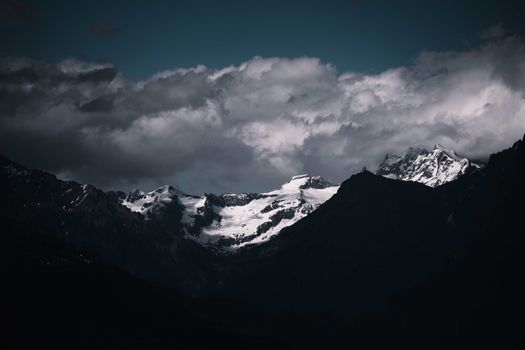 Captivating view of a snow-covered mountain range enveloped in dramatic clouds, showcasing nature's grandeur.