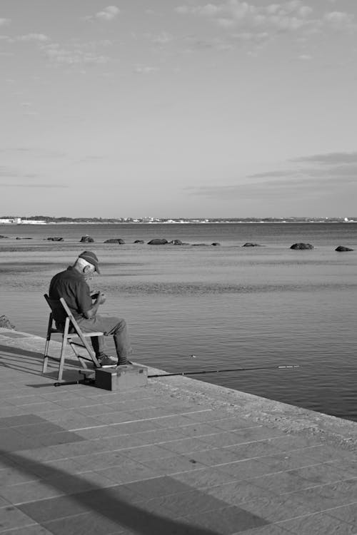 Elderly Man Sitting on a Wooden Chair fishing on the Riverside