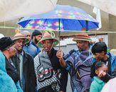 People wearing traditional attire celebrate with a colorful umbrella on a rainy day.