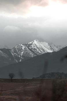 A dramatic landscape with snow-covered mountains beneath cloudy skies, evoking a moody atmosphere.