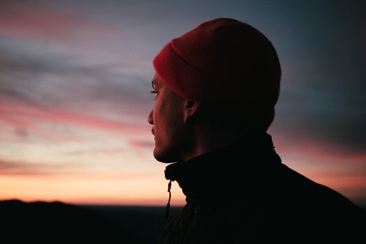A man in a beanie looks away, silhouetted against a colorful sunset in Deutschland.
