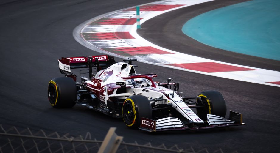 Foto dinâmica de um carro de Fórmula 1 correndo em uma pista moderna durante o dia.
