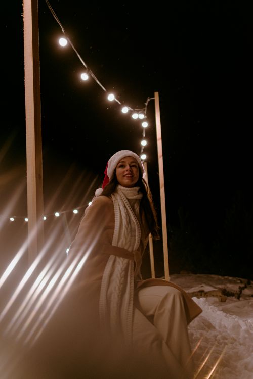 Free Woman in a Santa hat enjoys festive winter night with decorative lights. Stock Photo