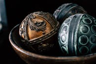 特写镜头展示了一个质朴木碗中设计复杂的装饰球体，体现了艺术金属制品的精湛工艺