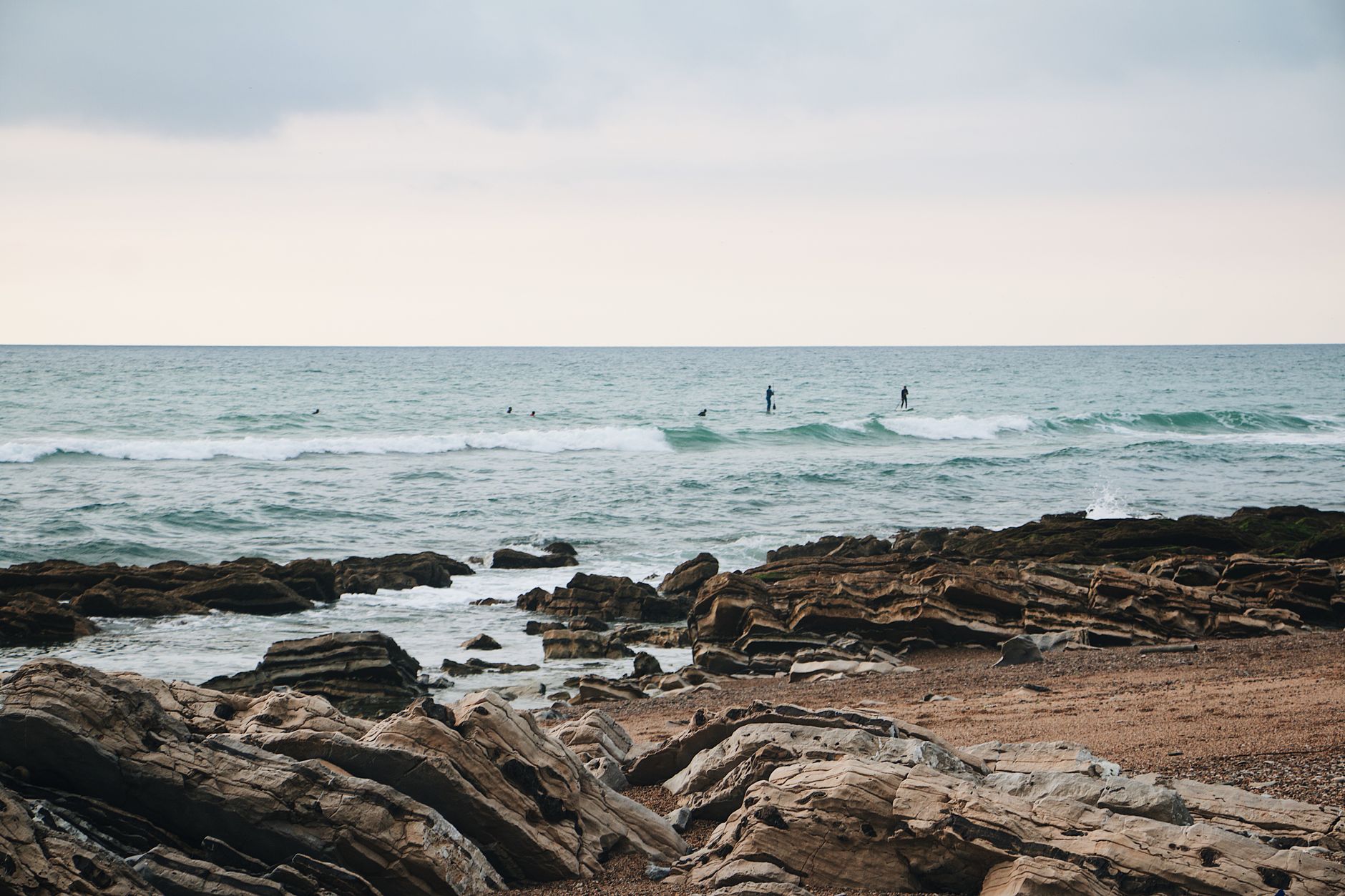 A serene view of paddleboarders on a rocky coastline under a cloudy sky.