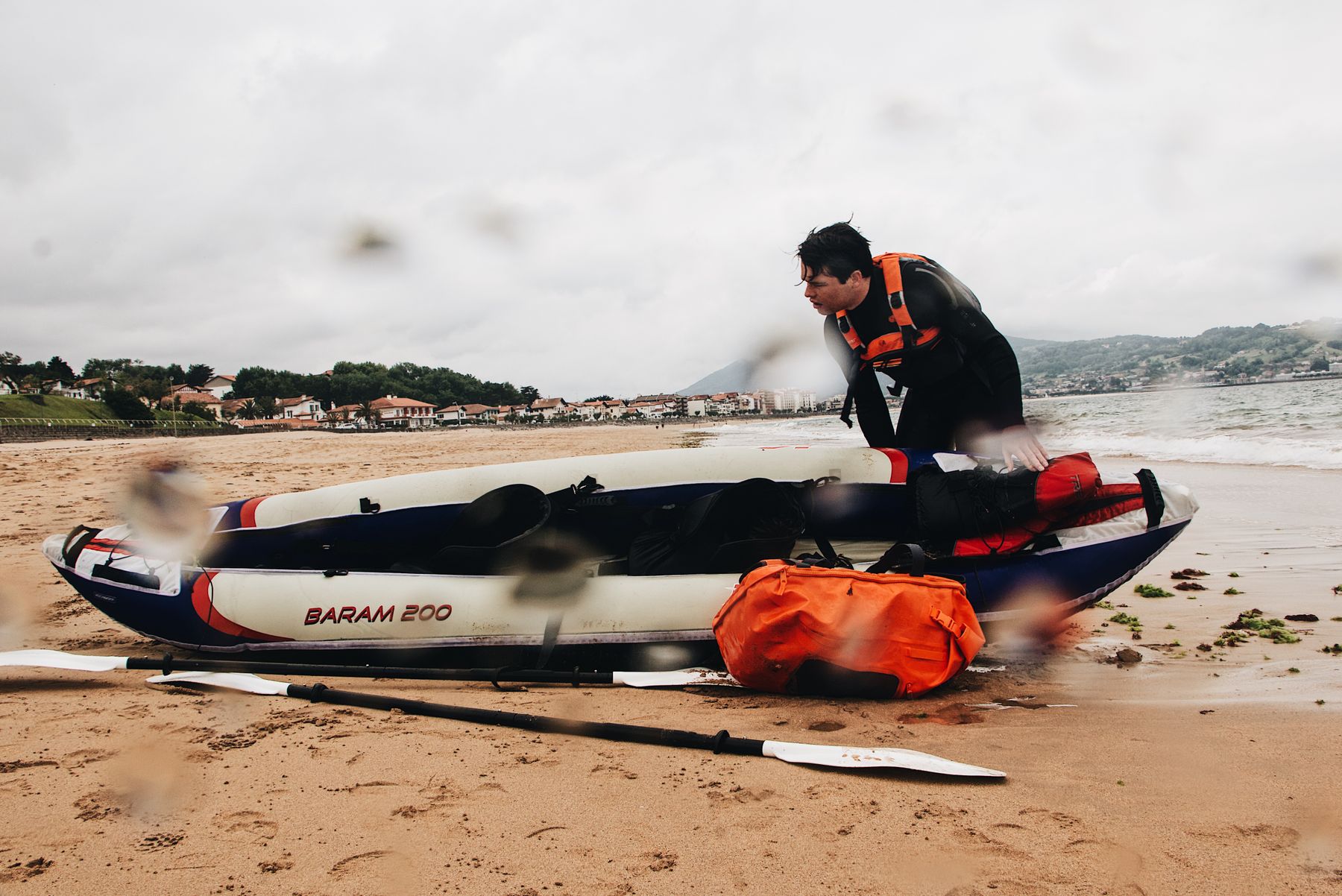 Kayaker preparing equipment beside a kayak on a sandy shoreline