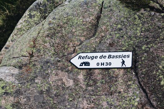 Close-up of a sign on a mossy boulder guiding hikers to Refuge de Bassies in 0H30.