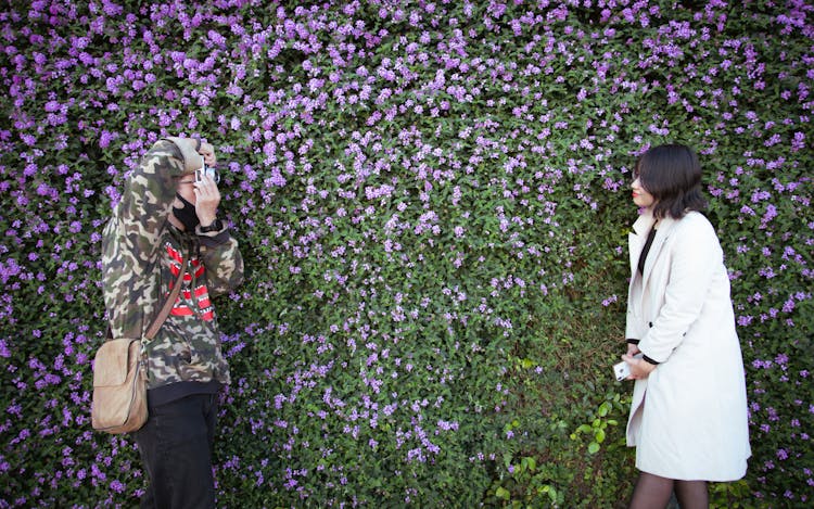 Man Photographing A Woman By A Bush With Purple Flowers