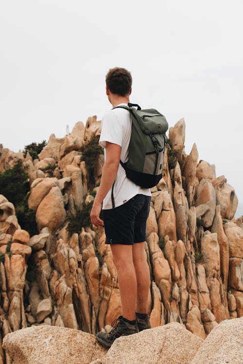 Free Man in White T-shirt and Black Shorts Standing Near Brown Rock Formation Stock Photo