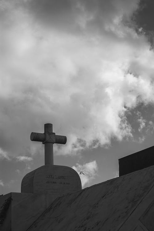 Grayscale Photo of a Cross Under Cloudy Sky