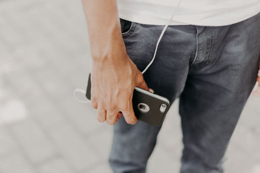 Close-up of a man holding a smartphone with headphones, showcasing modern tech and fashion.