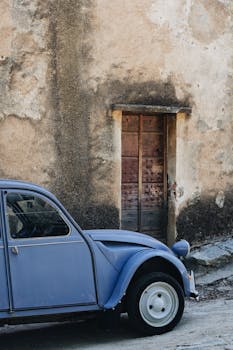 A classic blue vintage car parked beside an aged concrete wall, showcasing nostalgia.