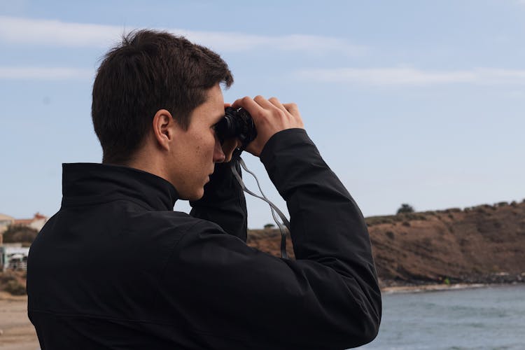 A Man In Black Jacket Using A Binoculars