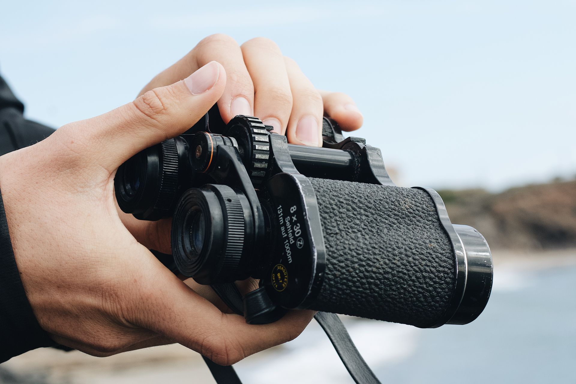 Close-up of hands holding binoculars outdoors, focusing on optical device details.