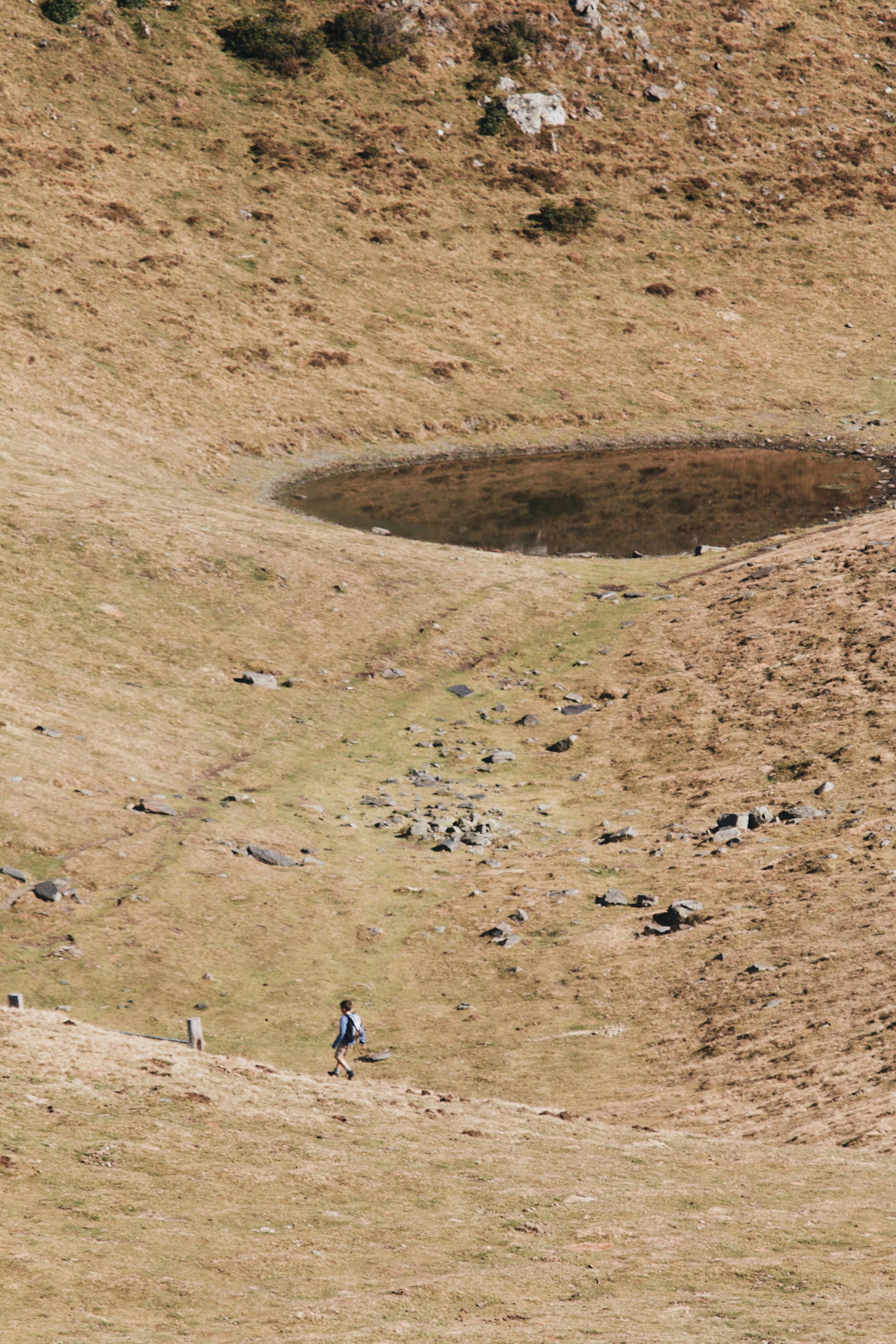 A lone hiker traverses a barren landscape with a small pond, capturing the essence of wilderness adventure.