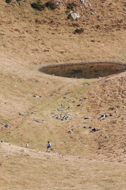 A lone hiker traverses a barren landscape with a small pond, capturing the essence of wilderness adventure.