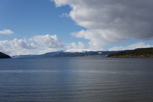 Peaceful lake scene with snowy mountains under a cloudy sky.
