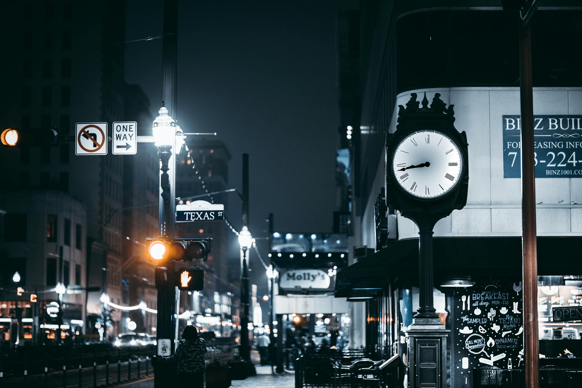 Vibrant city night scene on Texas St, featuring street clock and urban lights in Houston.