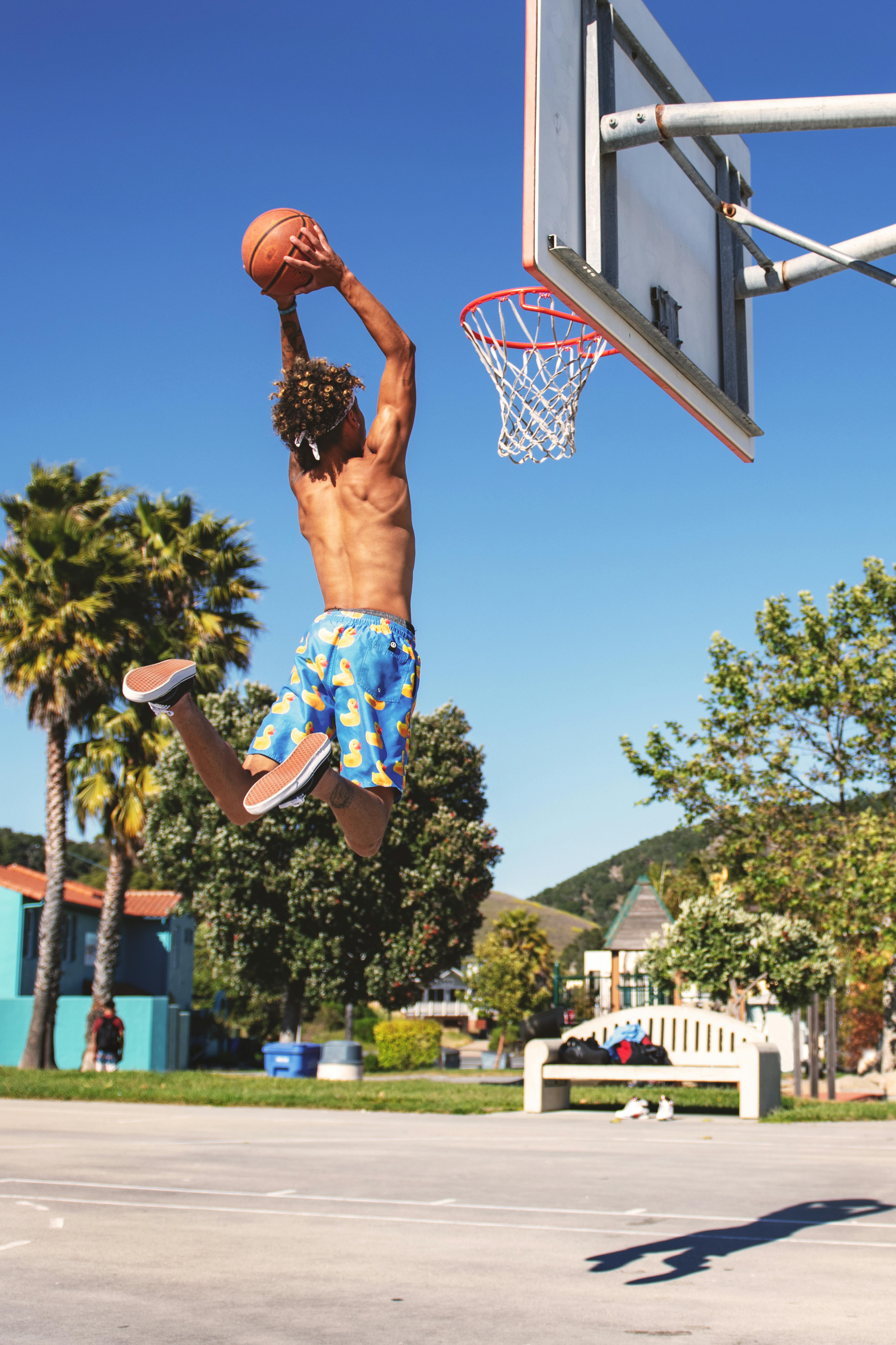Young man on basketball court, swinging on basketball net frame