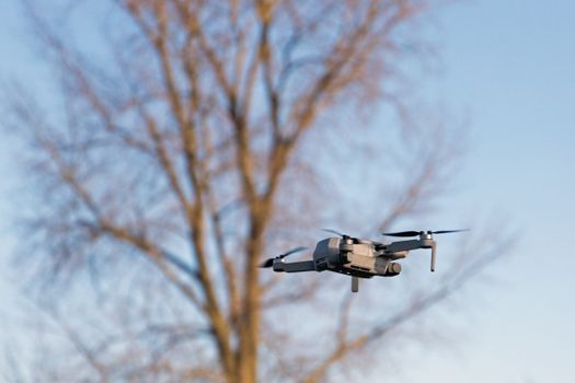 High-resolution image of a drone hovering with a clear sky and tree in the background.