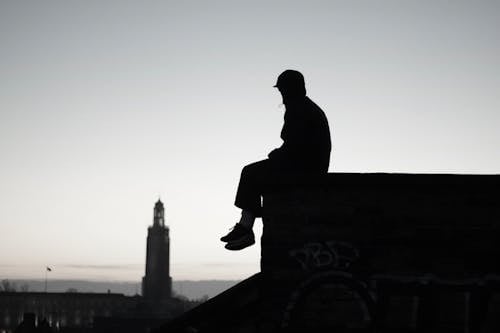 Silhouette of Man Sitting on a Gutter
