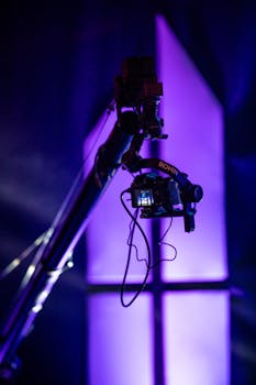 Dynamic shot of video camera mounted on a crane arm, silhouetted against purple lights.