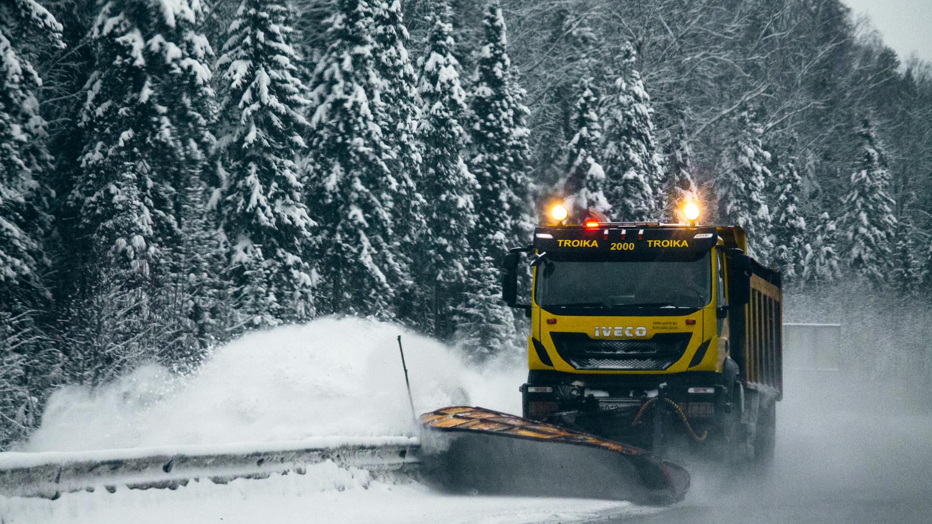 A bright snowplow clearing a snowy road through a winter forest, ensuring safe travel.