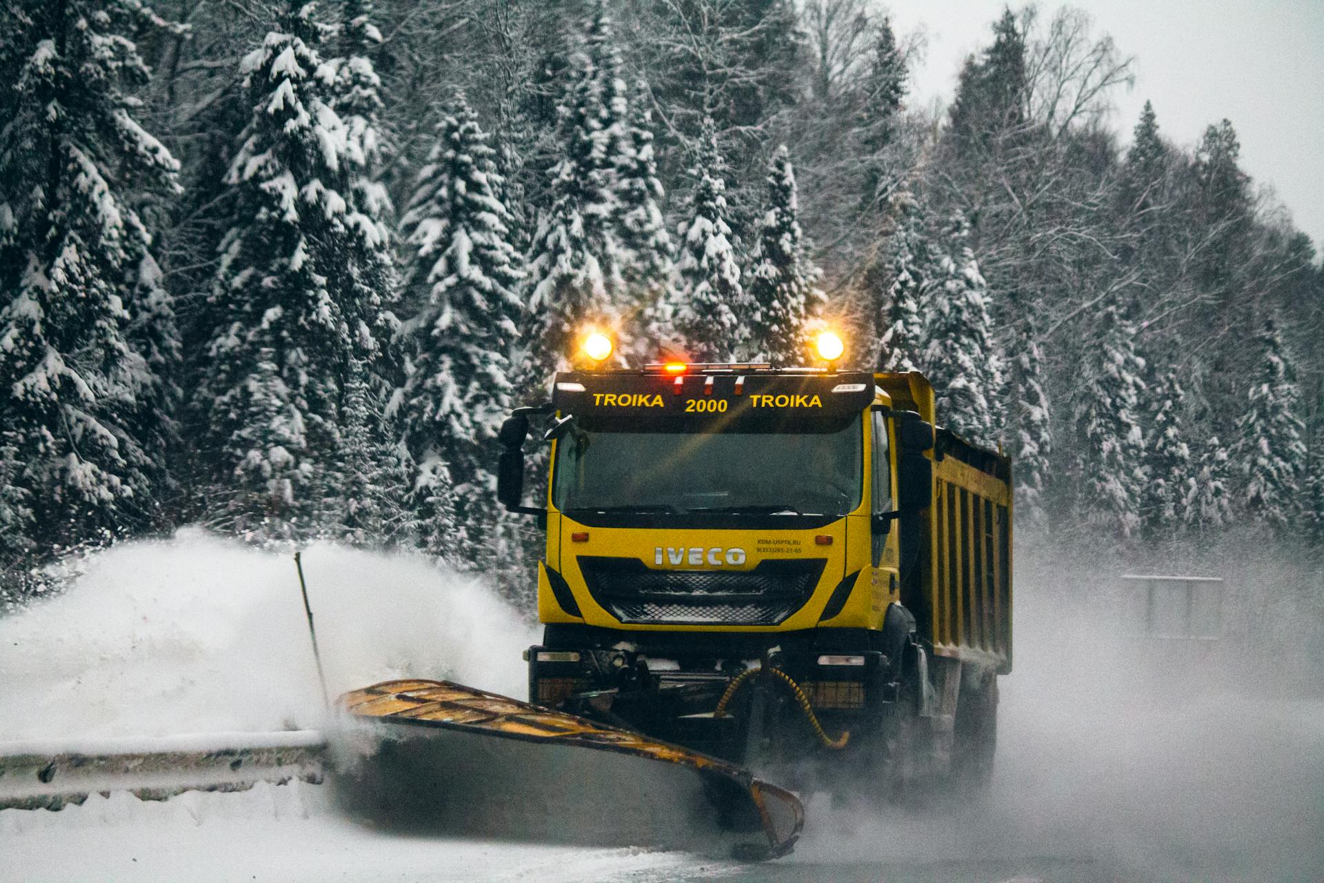 A yellow snowplow clearing a snow-covered road through a forest in winter