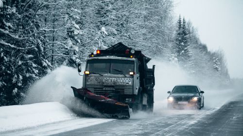 Free A snowplow clears a snowy road through a forest, enhancing winter driving safety. Stock Photo