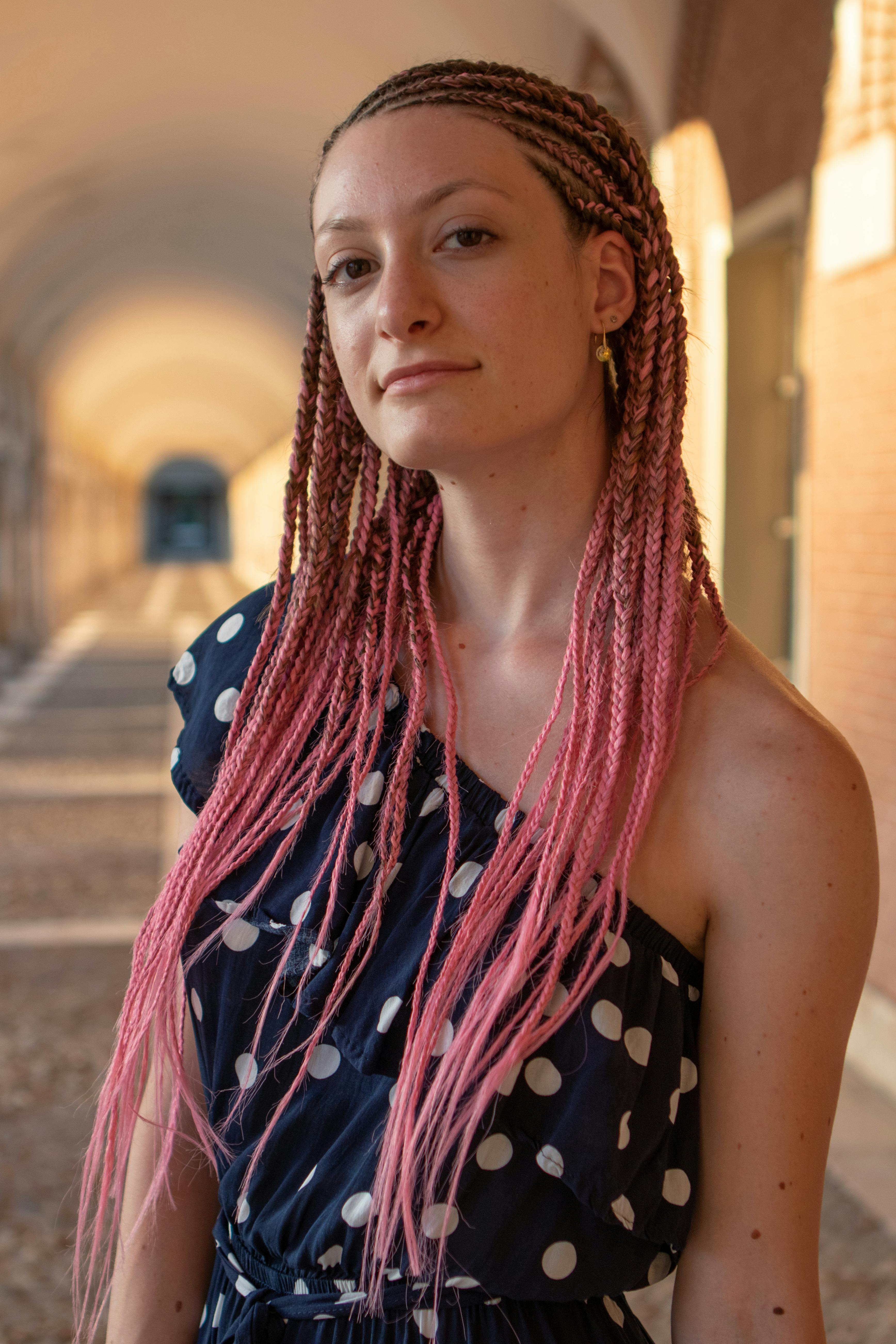 Stylish young woman with pink braided hair in a polka dot dress standing outdoors.