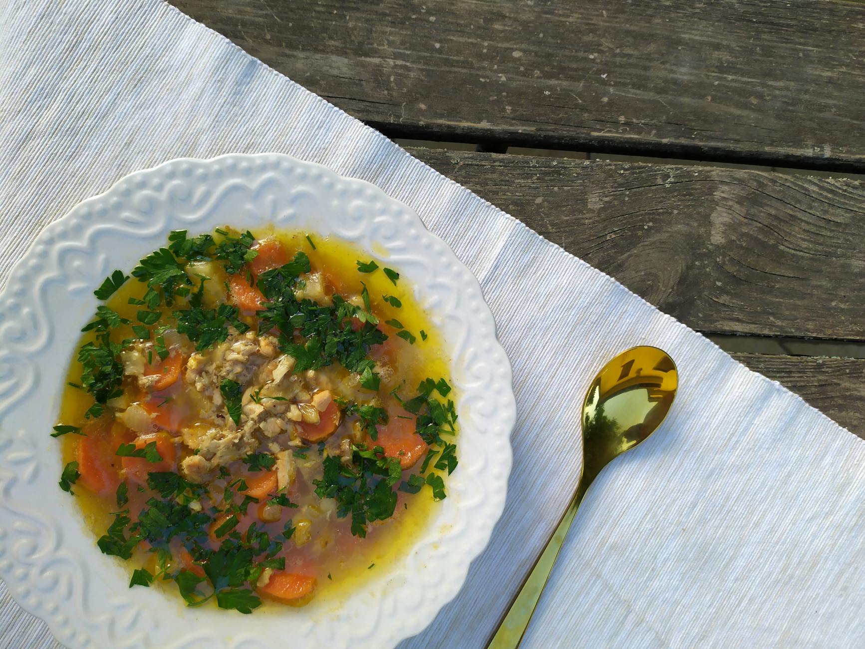 Delicious homemade chicken soup garnished with fresh parsley, served on a rustic table setting.