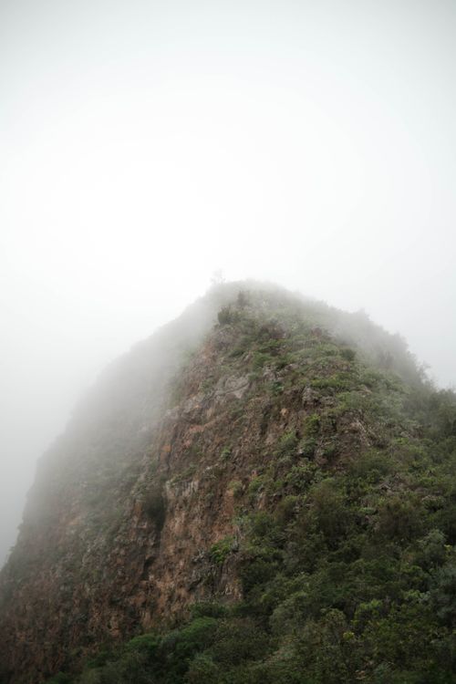 Free A dramatic misty mountain peak partially obscured by dense fog, creating an ethereal landscape. Stock Photo