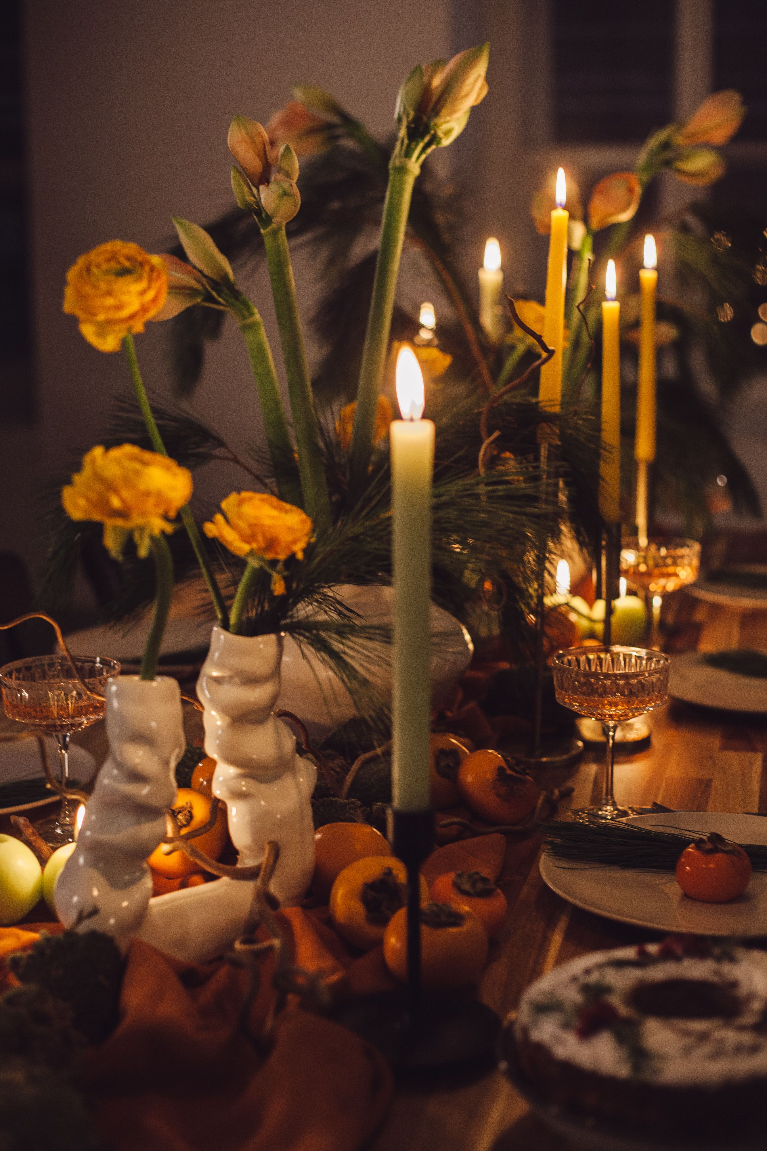 Elegant dining table with candles, orange flowers, and autumn fruits creating a warm ambiance.