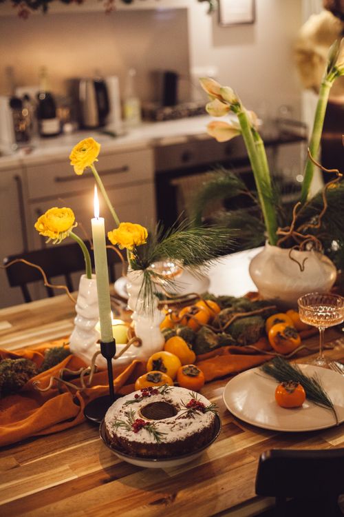 Free Cozy festive table setting with cake, candles, and floral decorations for a holiday celebration. Stock Photo
