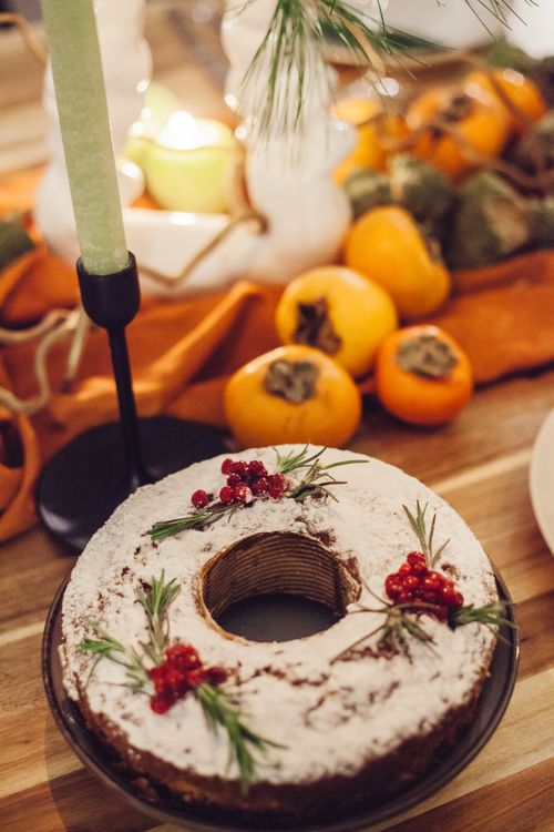 Free A beautifully decorated holiday cake garnished with berries and fresh herbs, surrounded by seasonal persimmons. Stock Photo