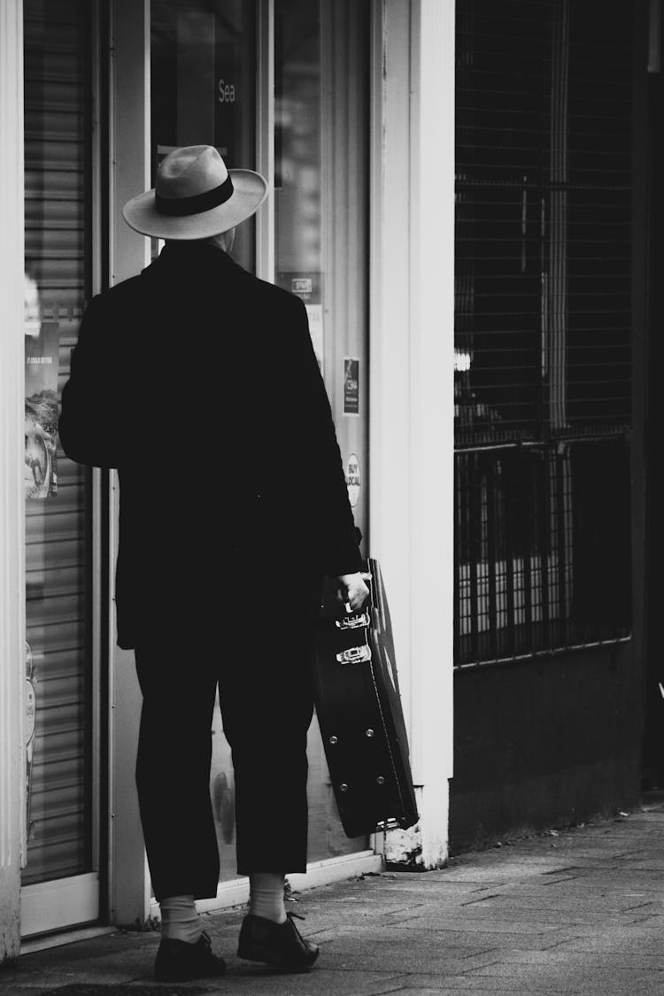 Back View Man In Black Suit Carrying A Guitar Case