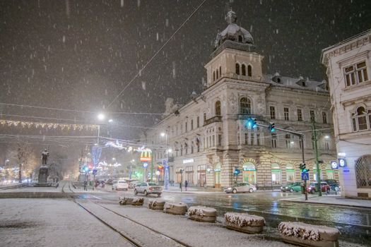 A snowy winter night scene in Arad, Romania, showcasing historic buildings under festive lights.
